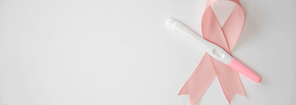 Prueba de embarazo colocada sobre un lazo rosa, símbolo de la lucha contra el cáncer de mama, sobre fondo blanco. La imagen representa la esperanza de la maternidad después de superar un tratamiento oncológico