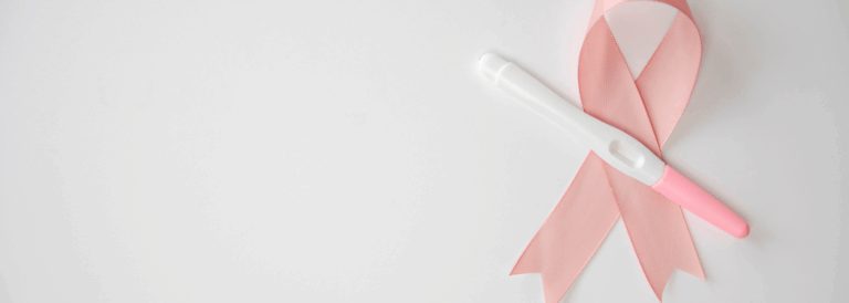 Prueba de embarazo colocada sobre un lazo rosa, símbolo de la lucha contra el cáncer de mama, sobre fondo blanco. La imagen representa la esperanza de la maternidad después de superar un tratamiento oncológico