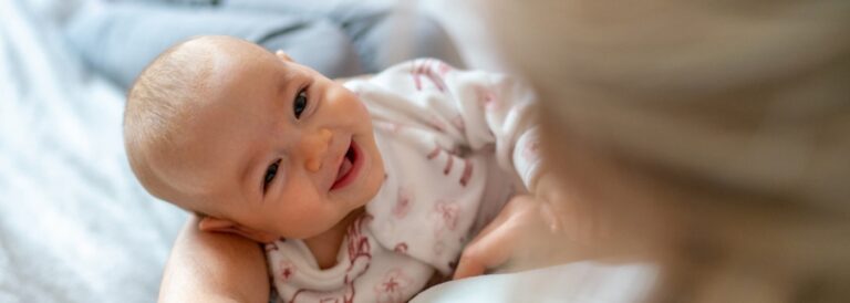 Bebê sorrindo nos braços da mãe, transmitindo afeto e conexão durante o cuidado.