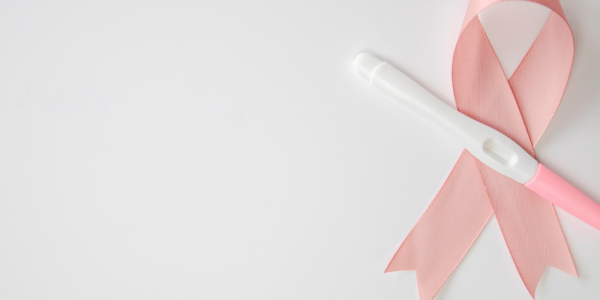 Prueba de embarazo colocada sobre un lazo rosa, símbolo de la lucha contra el cáncer de mama, sobre fondo blanco. La imagen representa la esperanza de la maternidad después de superar un tratamiento oncológico